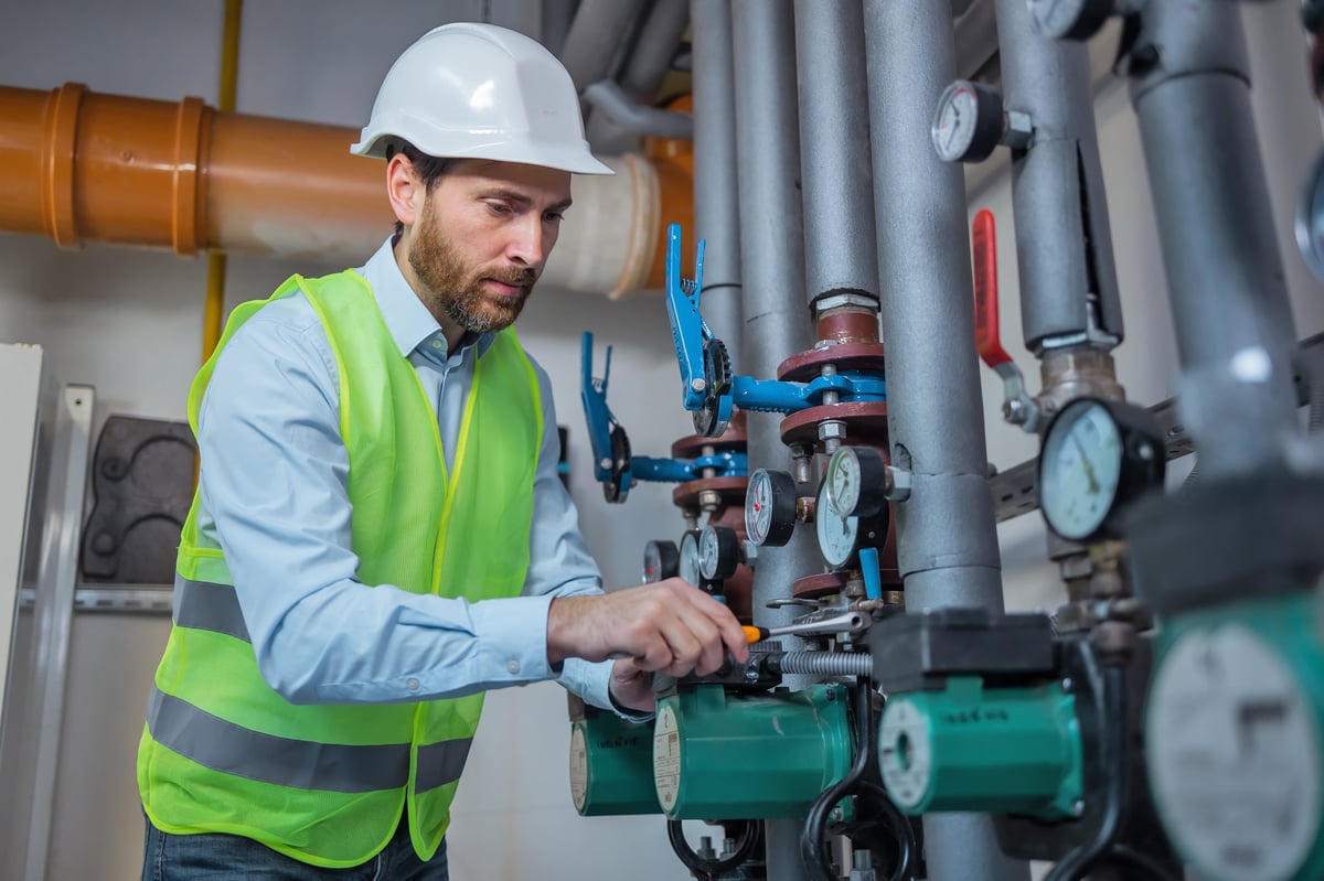 Technician adjusting water flow through pipes in a commercial boiler room