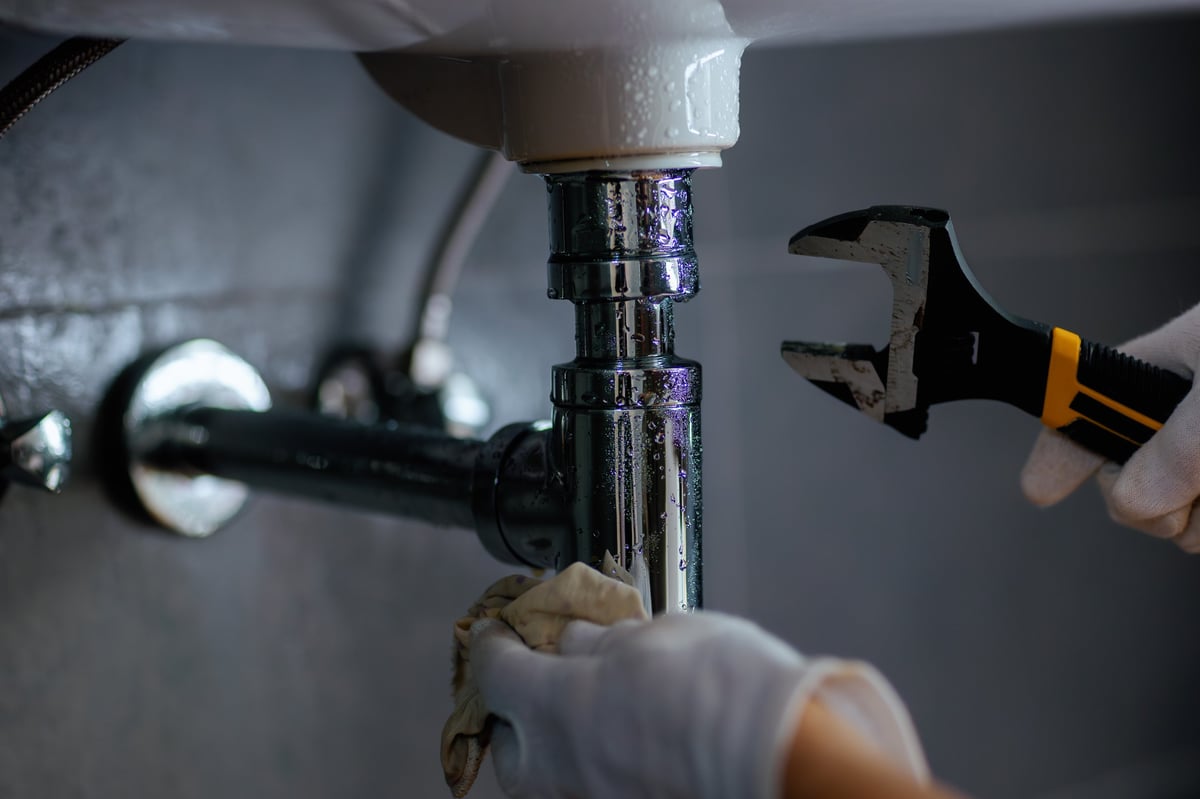 Technician in white gloves servicing chrome plumbing fittings under a sink